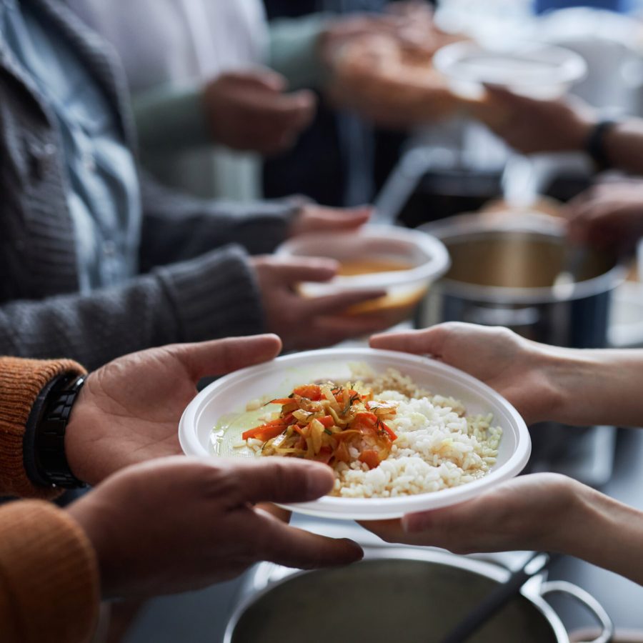 Close up of hands holding plastic plate with rice, unrecognizable volunteer helping refugees at soup kitchen